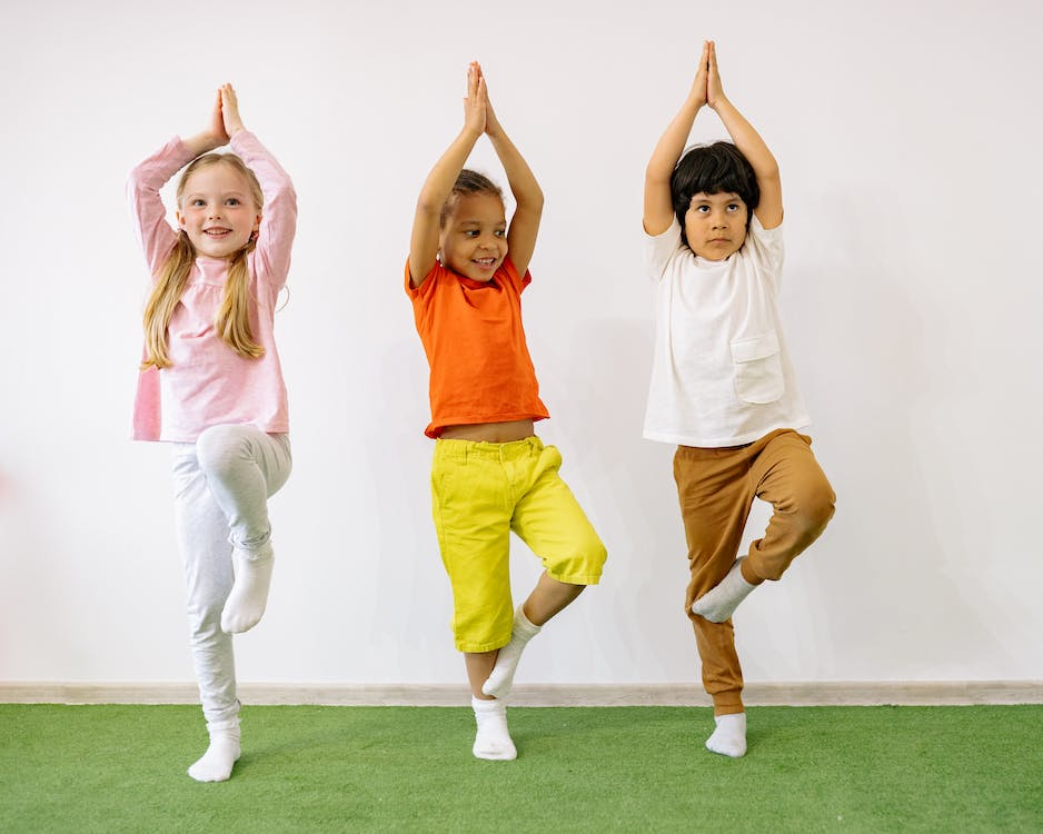 Three children standing on one leg in their classroom.