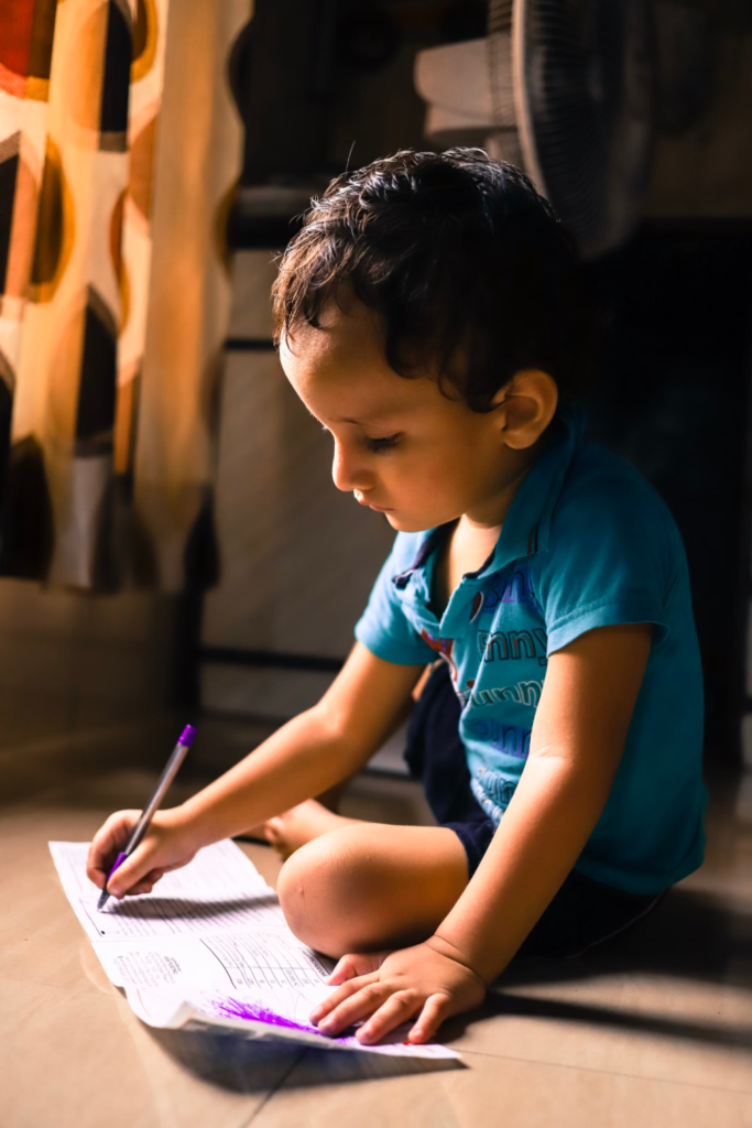 A child works in a book while sitting on the floor.