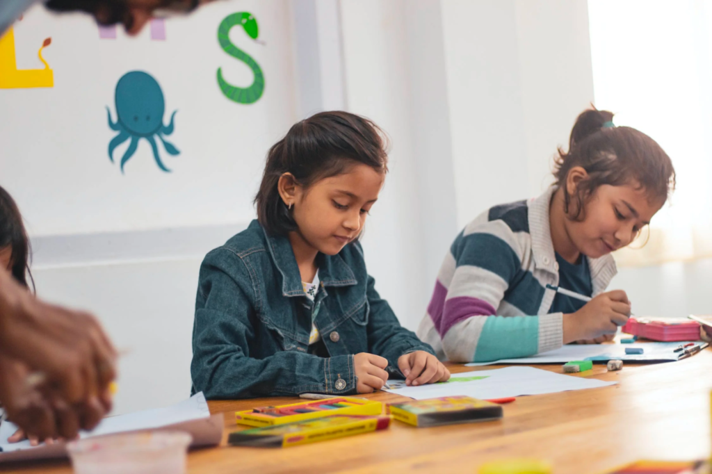 A young, shy girl colors while sitting in a classroom. 