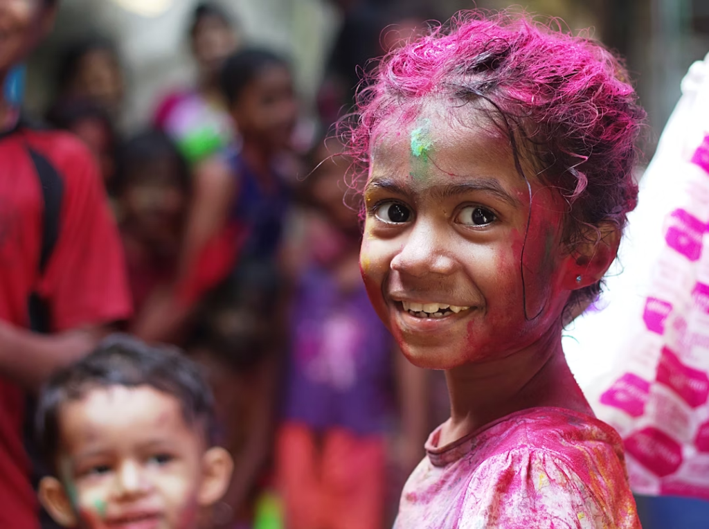  A young girl enjoys Holi while smiling at the camera.