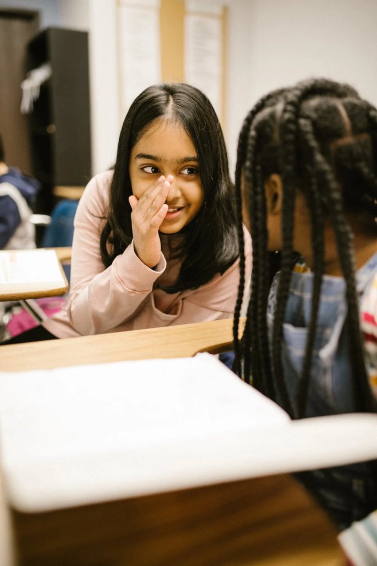 Two students whisper and talk in a classroom.