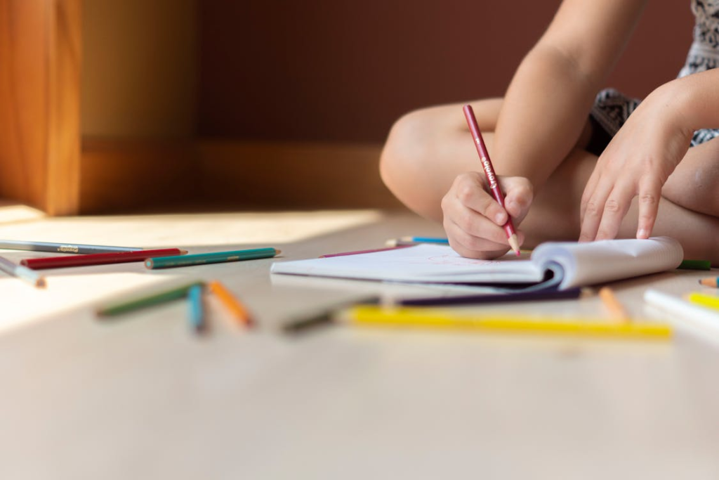 A kid sitting on the floor with his book and pencils