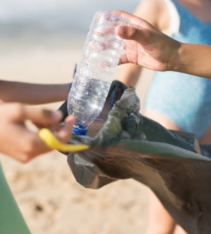 A hand placing an empty plastic bottle into a black garbage bag during a clean-up drive