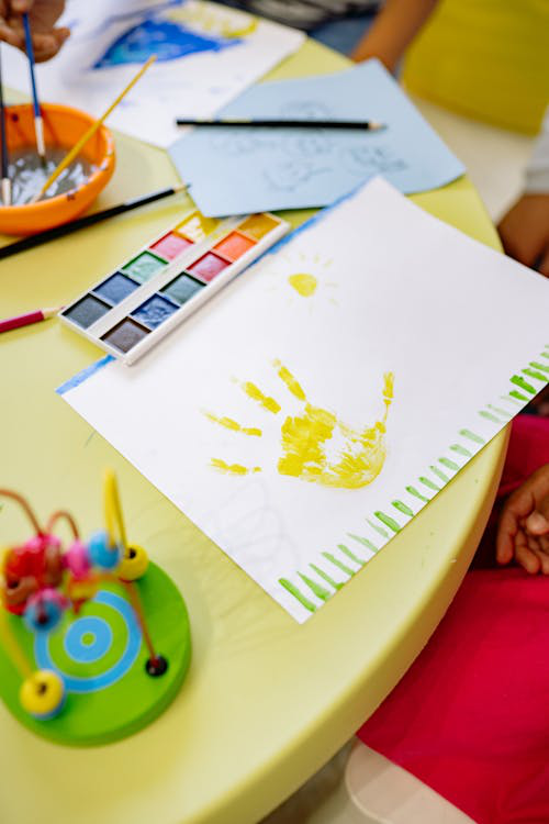 Art materials and a painting of a hand on a table, symbolizing creativity and expression in children’s learning