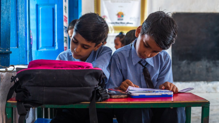 Two boys sitting at a desk with books, engaging in learning activities